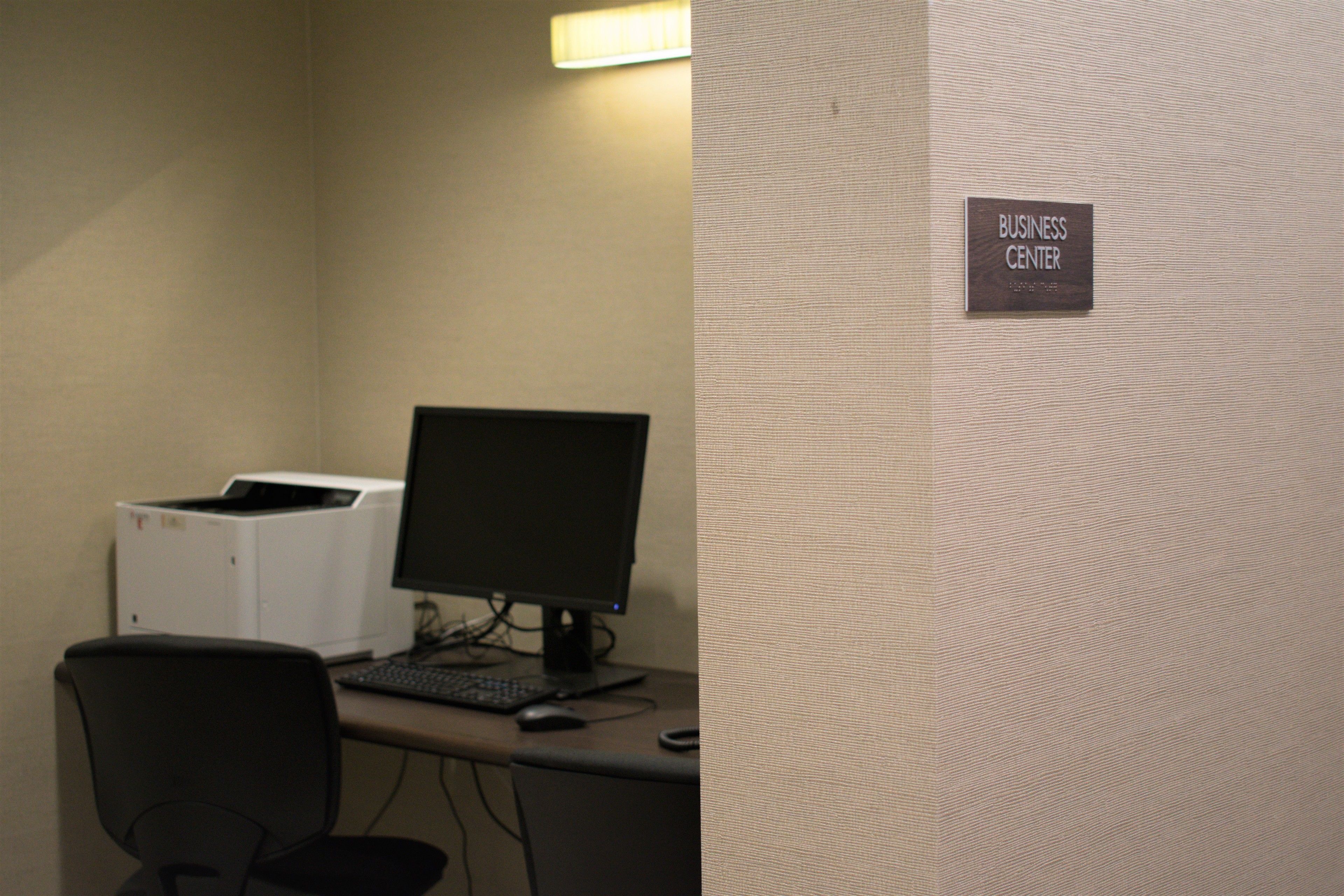 A business center with a computer desk, monitor, keyboard, and printer.