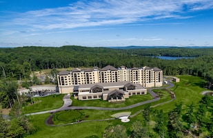 Un hotel grande con varias edificaciones, rodeado de césped verde y árboles, con un lago al fondo.