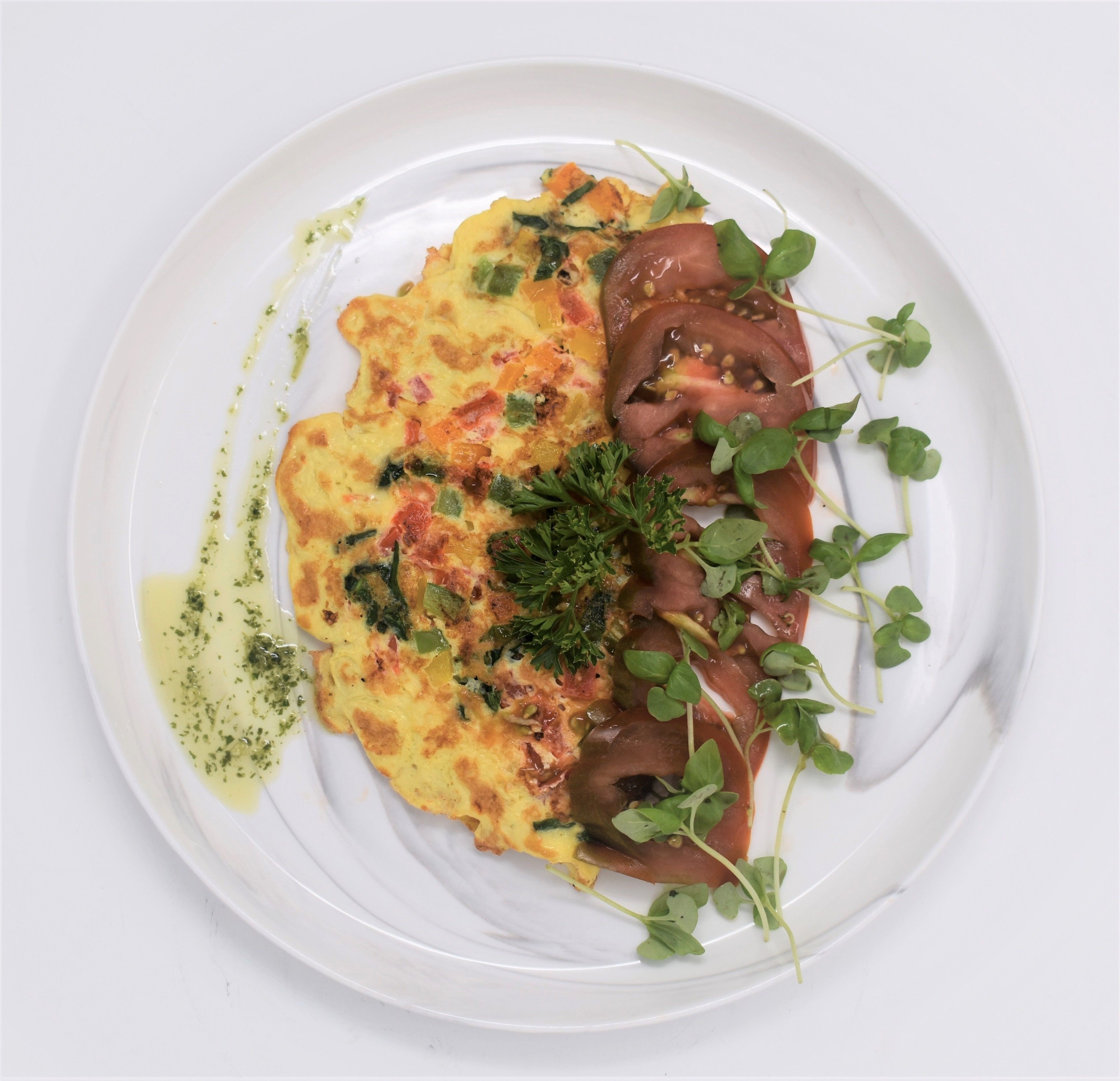 A white plate with a frittata, greens, and tomato slices.