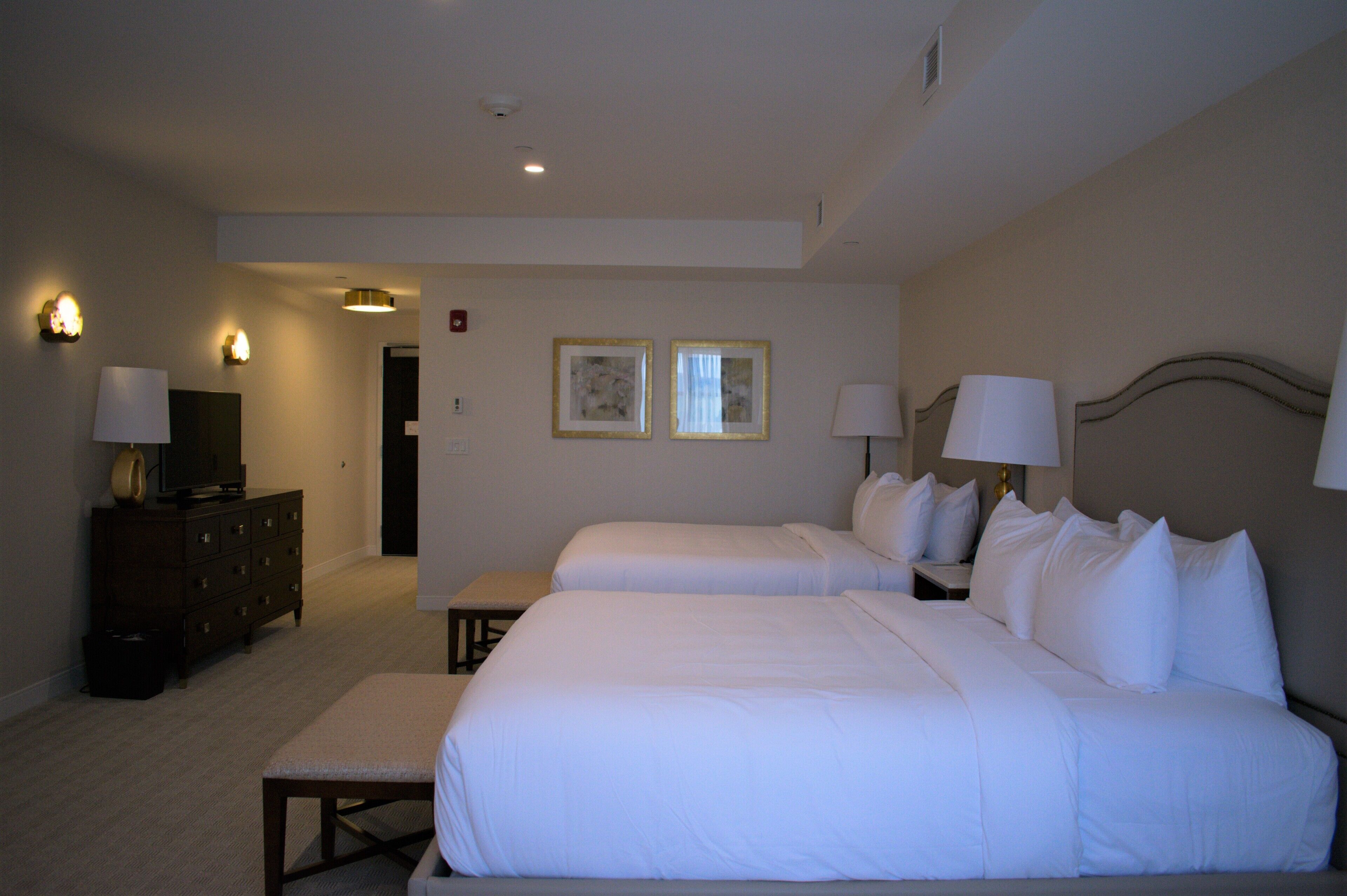 A hotel room with two beds, a dresser, a television, and two wall-mounted lamps.
