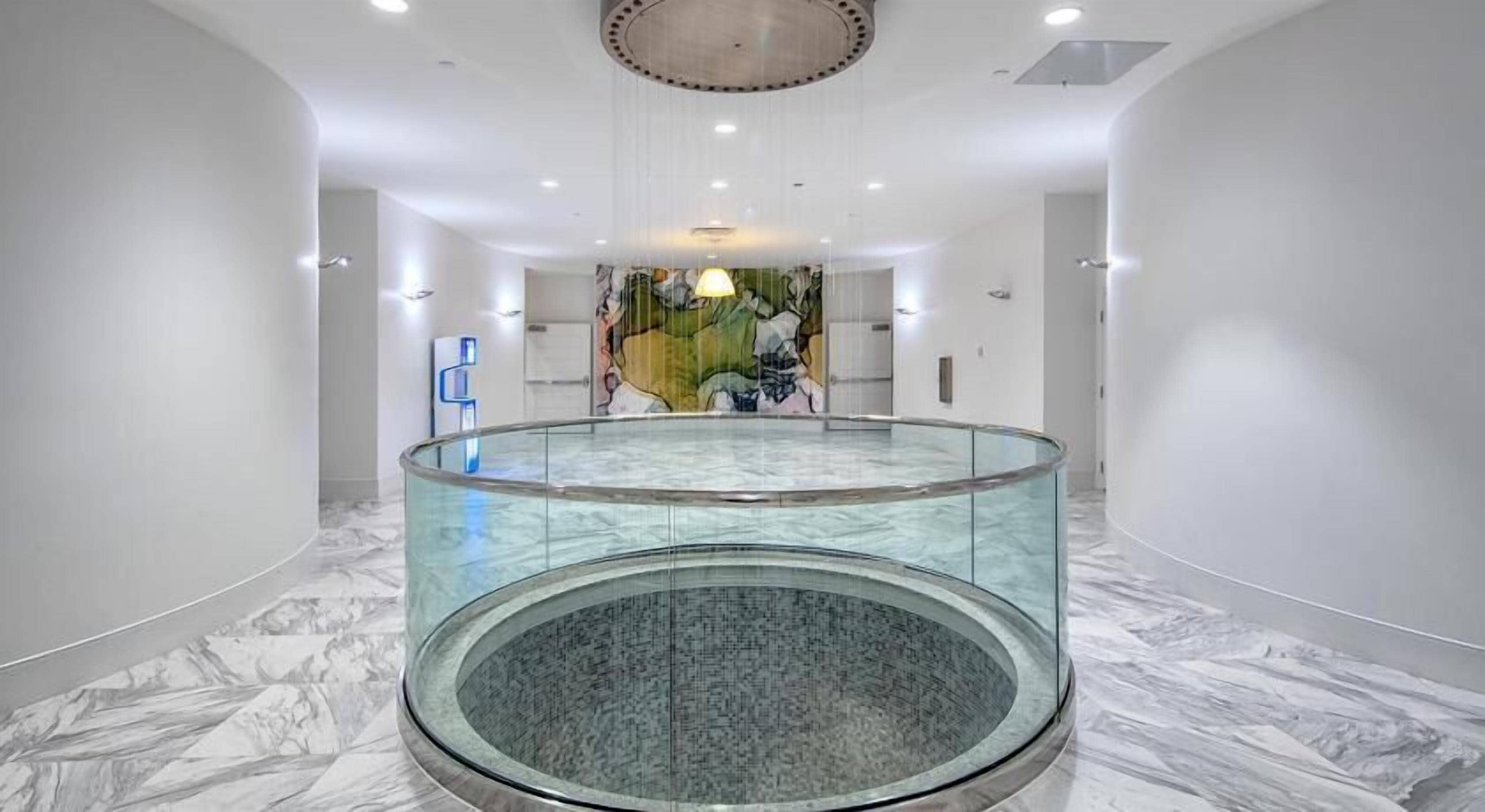 A modern hotel lobby with a circular glass railing, marble flooring, and a central art installation.