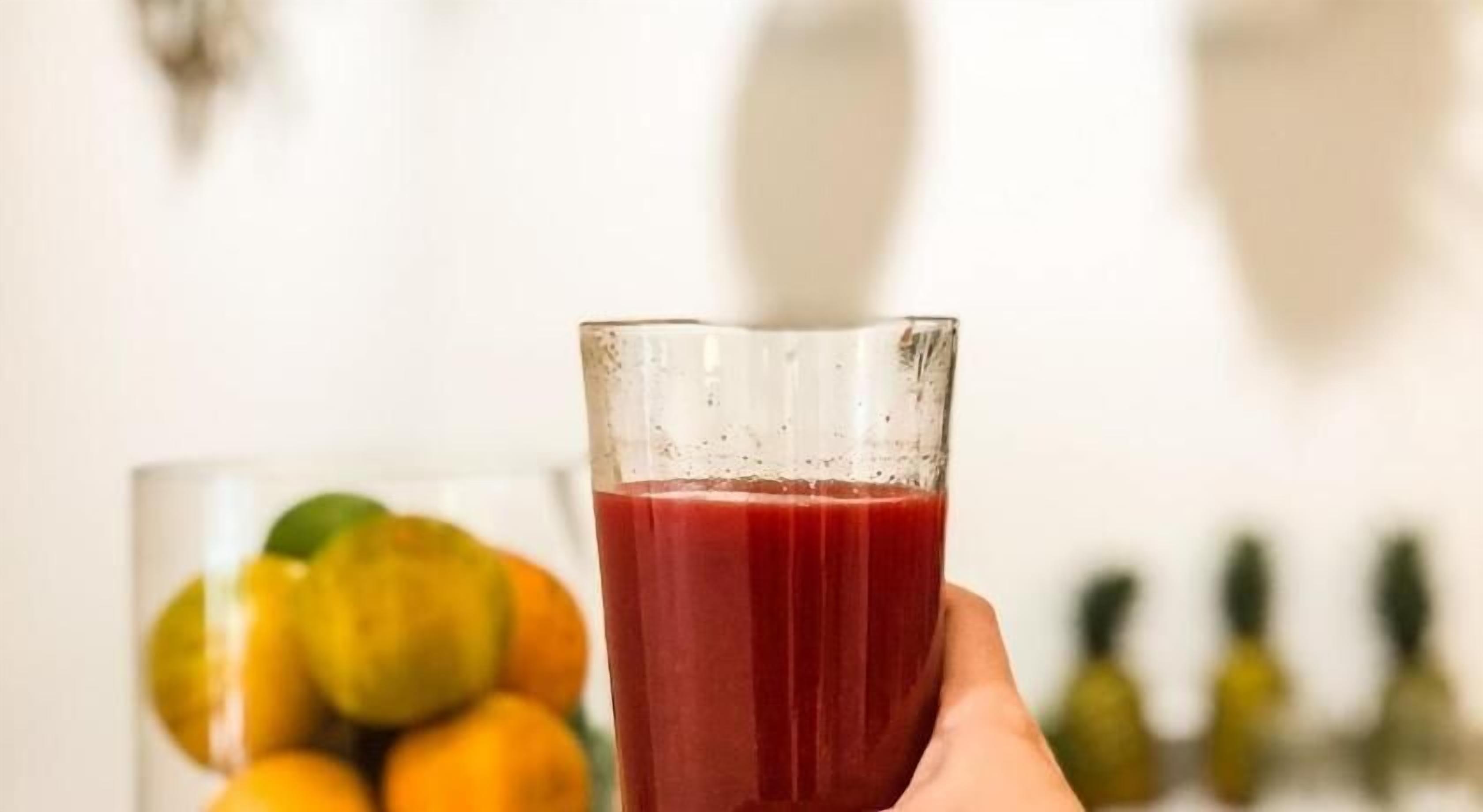 Une main tenant un verre de jus rouge, avec un arrière-plan flou de fruits.