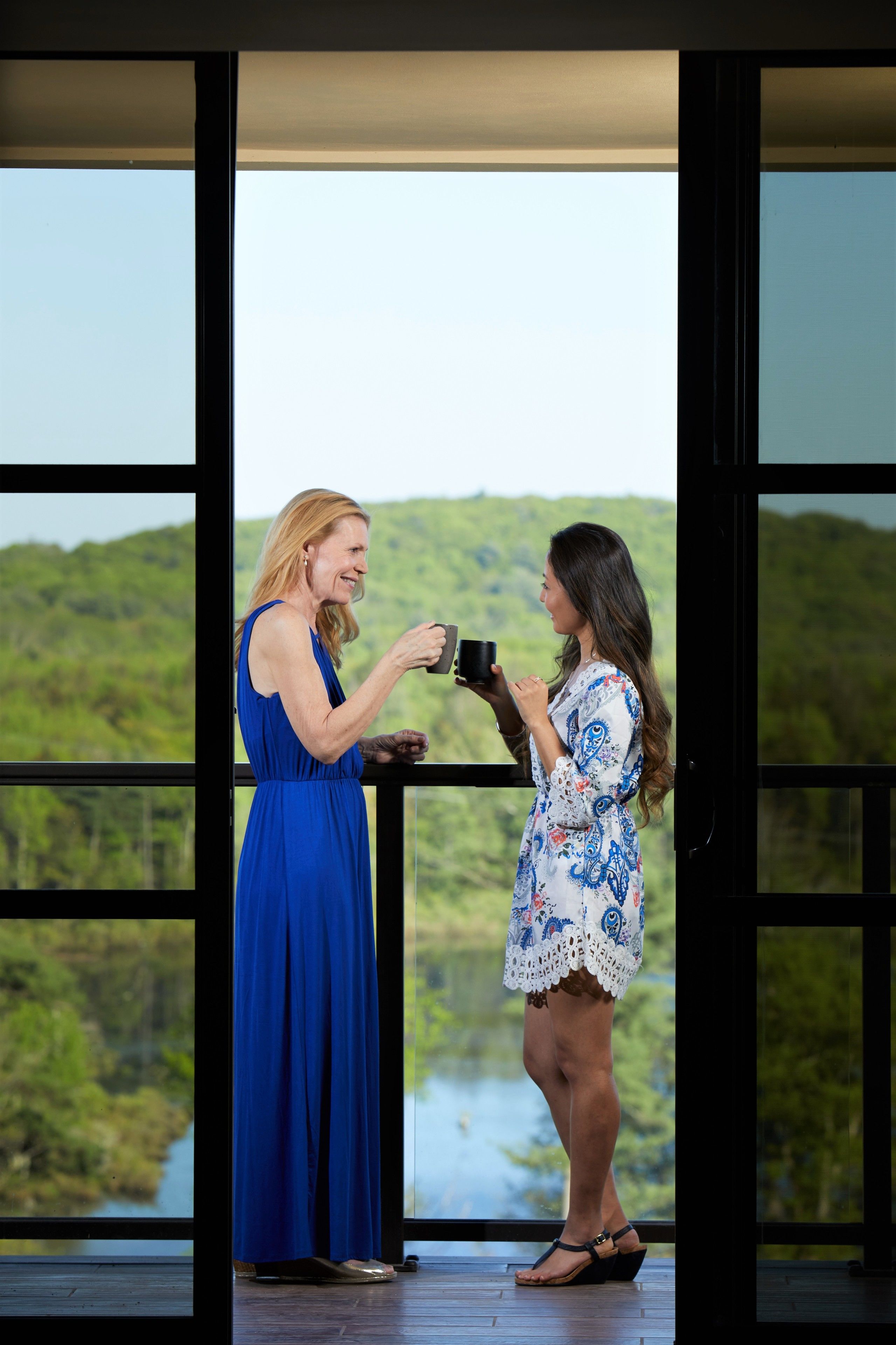Two women standing by a balcony with a scenic view of a lake and hills.