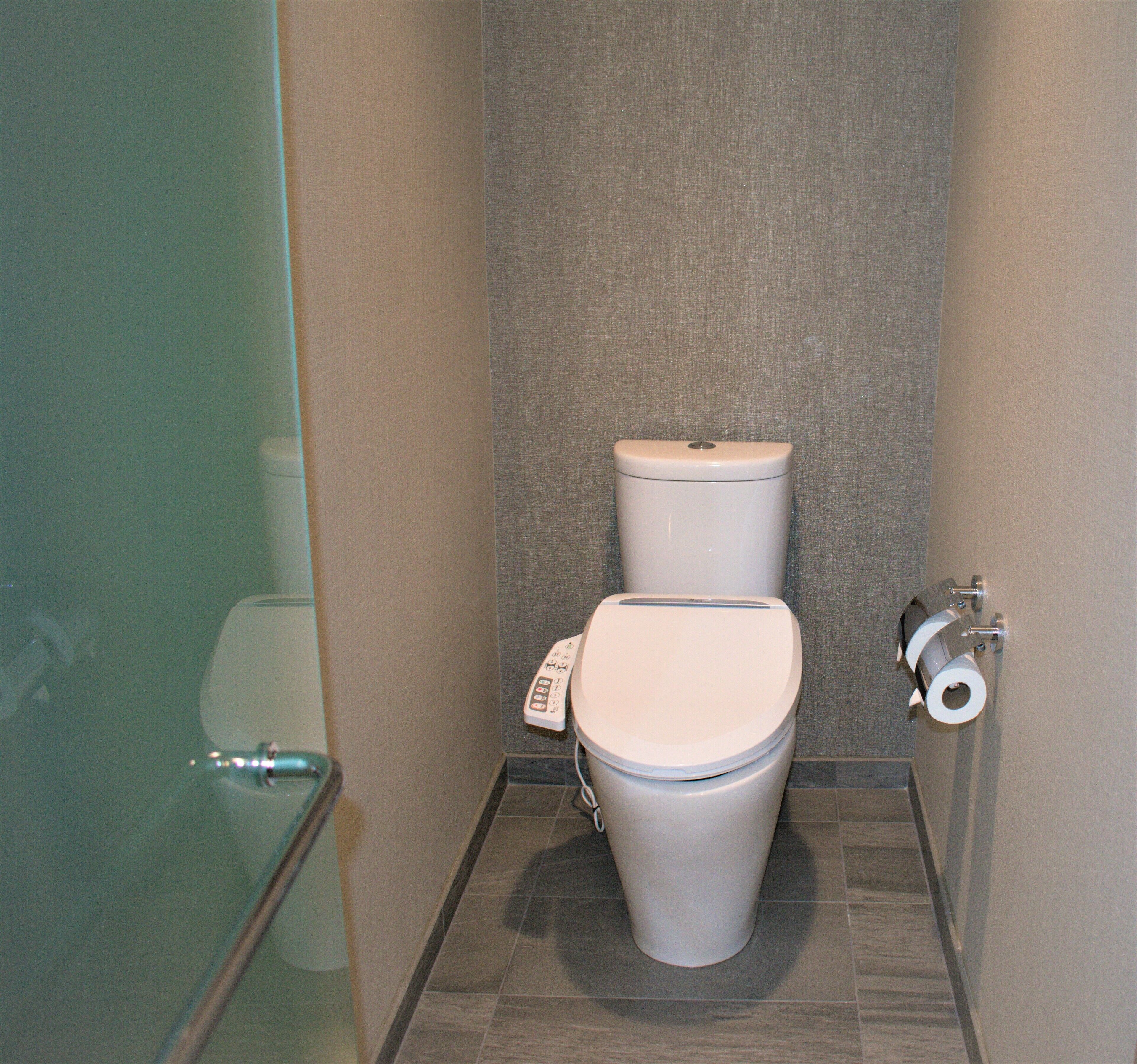 Een compacte, moderne badkamer met toilet, een douchecabine van glas en een toiletrolhouder aan de muur.