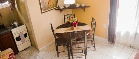 A dining area with a round table, chairs, a vase with flowers, a hanging lamp, and a painting on the wall.