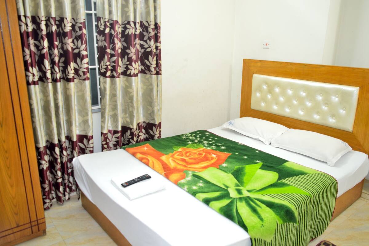 A bed with a floral bedspread, a wooden headboard, and a remote control on the bed.