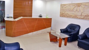 A reception area with a wooden reception desk, a glass table, and blue leather chairs. - Hotel Pink Shore (Cox's Bazar)