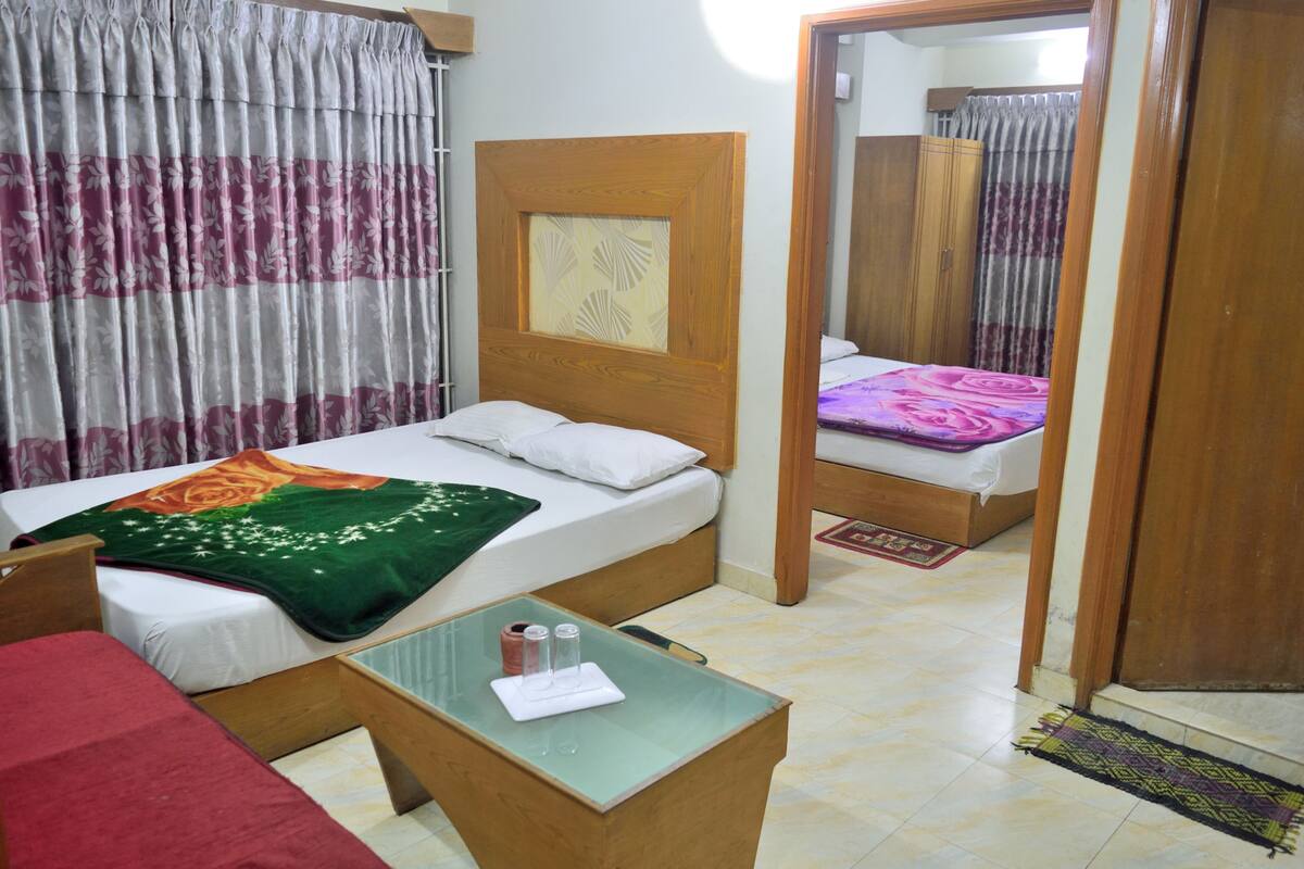 A hotel room with a bed, a small table with a tray, a chair, a wooden headboard, and a mirror.