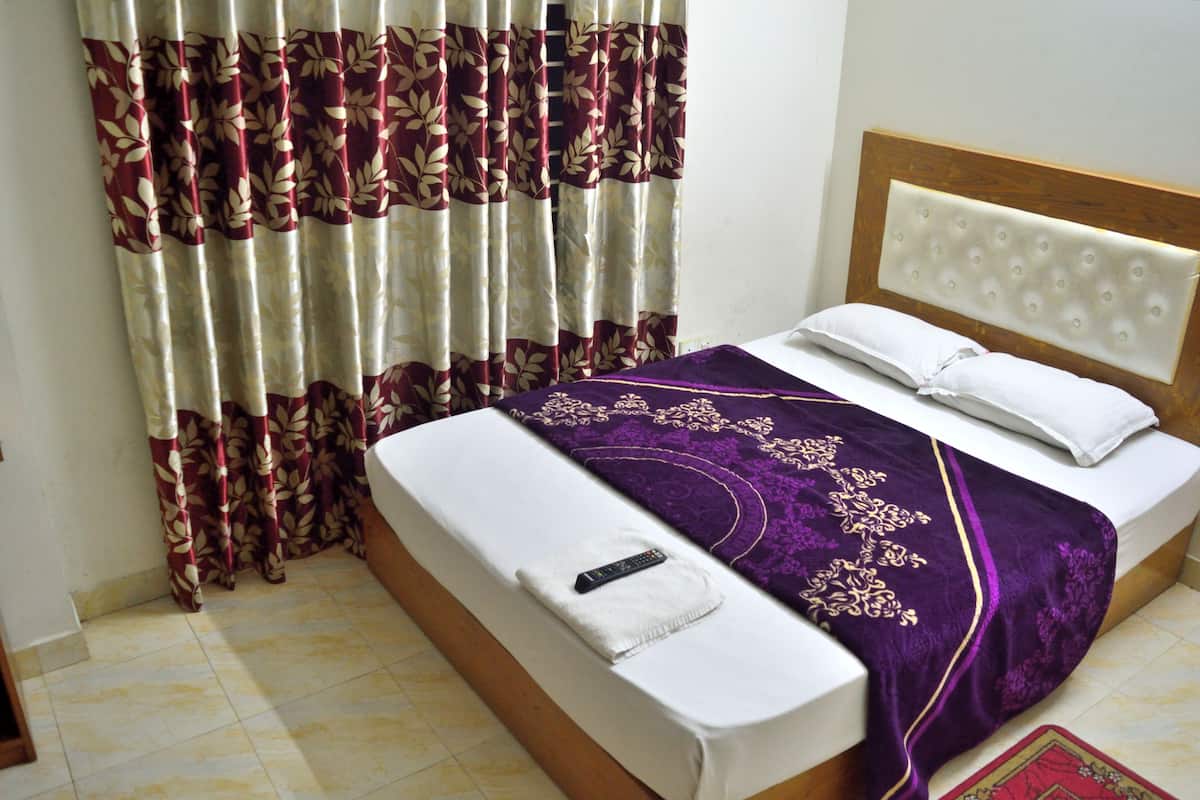 A bed with a white mattress, a purple blanket, and a remote control on the side.