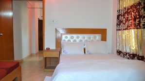 A hotel room with a large bed, a wooden headboard, a nightstand, and a red chair. - Hotel Pink Shore (Cox's Bazar)