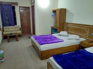 A bedroom with a bed, a wooden wardrobe, a small table, a chair, and a window with curtains.