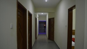 Un pasillo estrecho con puertas de madera a ambos lados, que da a una habitación con cama y una colcha roja.