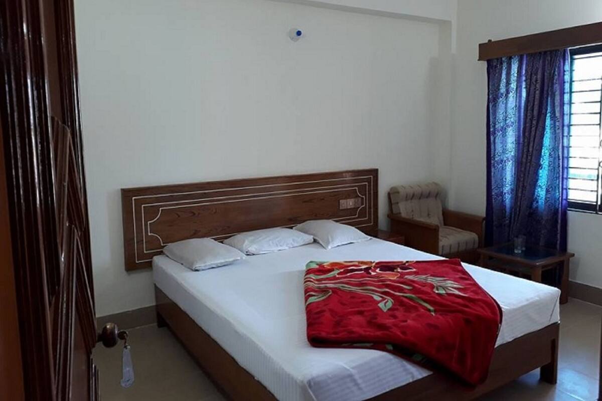 A bedroom with a wooden bed, white bedding, a red blanket, a chair, and a window with curtains.