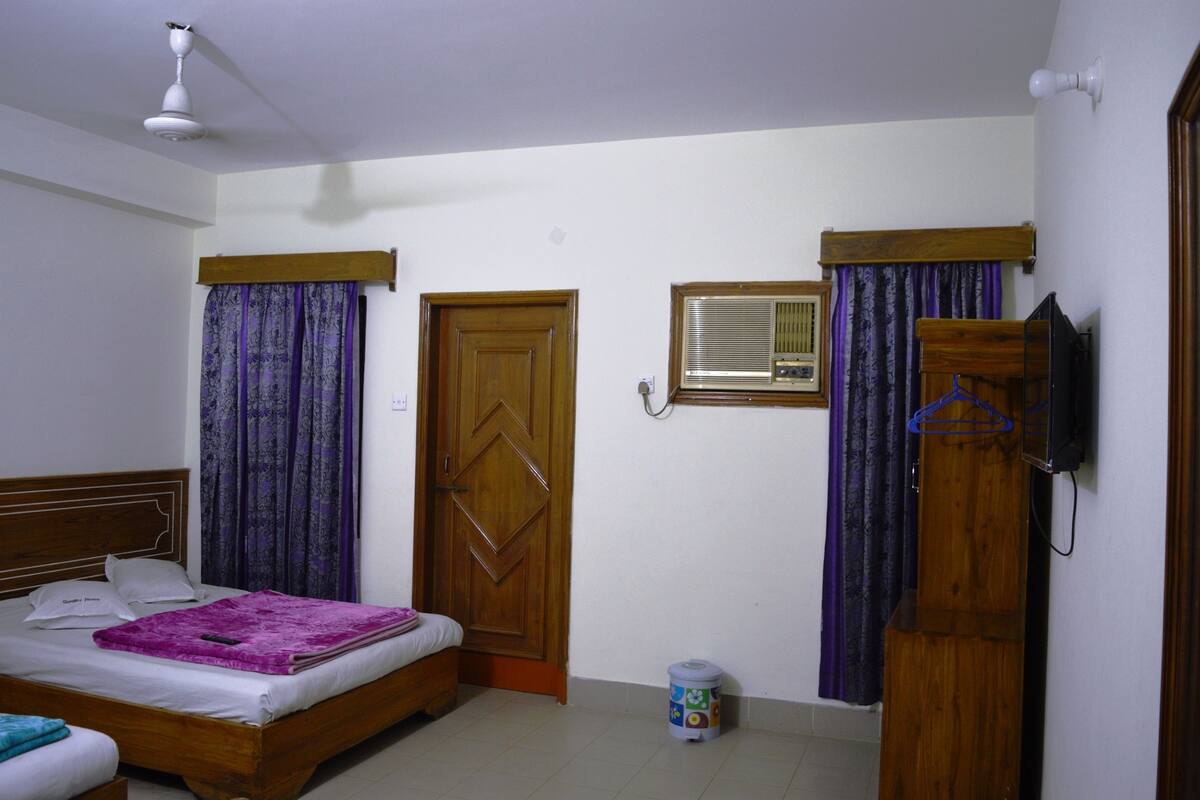 A bedroom with a bed, curtains, a wooden door, a ceiling fan, and a wall-mounted air conditioning unit.