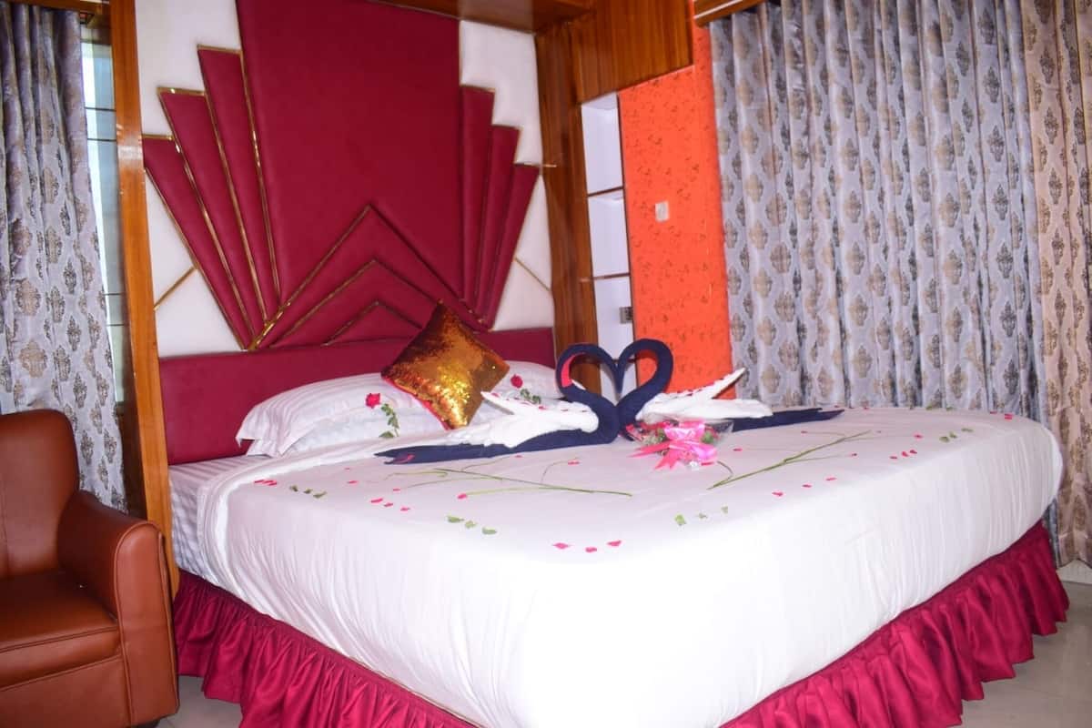 A neatly made bed with a white bedspread, red curtains, and a brown leather chair.