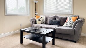 A living room with a grey sofa, a black coffee table, and two windows with blinds. - Ace Vacation Home at Niagara Falls - Canada (Niagara Falls)