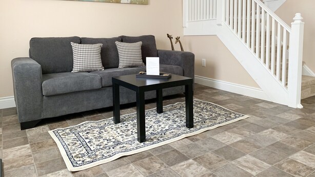 A living room with a gray sofa, patterned cushions, a black coffee table, a decorative rug, a painting on the wall, and a white staircase. - Ace Vacation Home at Niagara Falls - Canada (Niagara Falls)