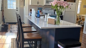 A kitchen with a central island, wooden bar stools, pendant lights, and a ceiling fan. - Charming Beach Bungalow Near Everything. 3BR, 2 bath.  (Old Orchard Beach)