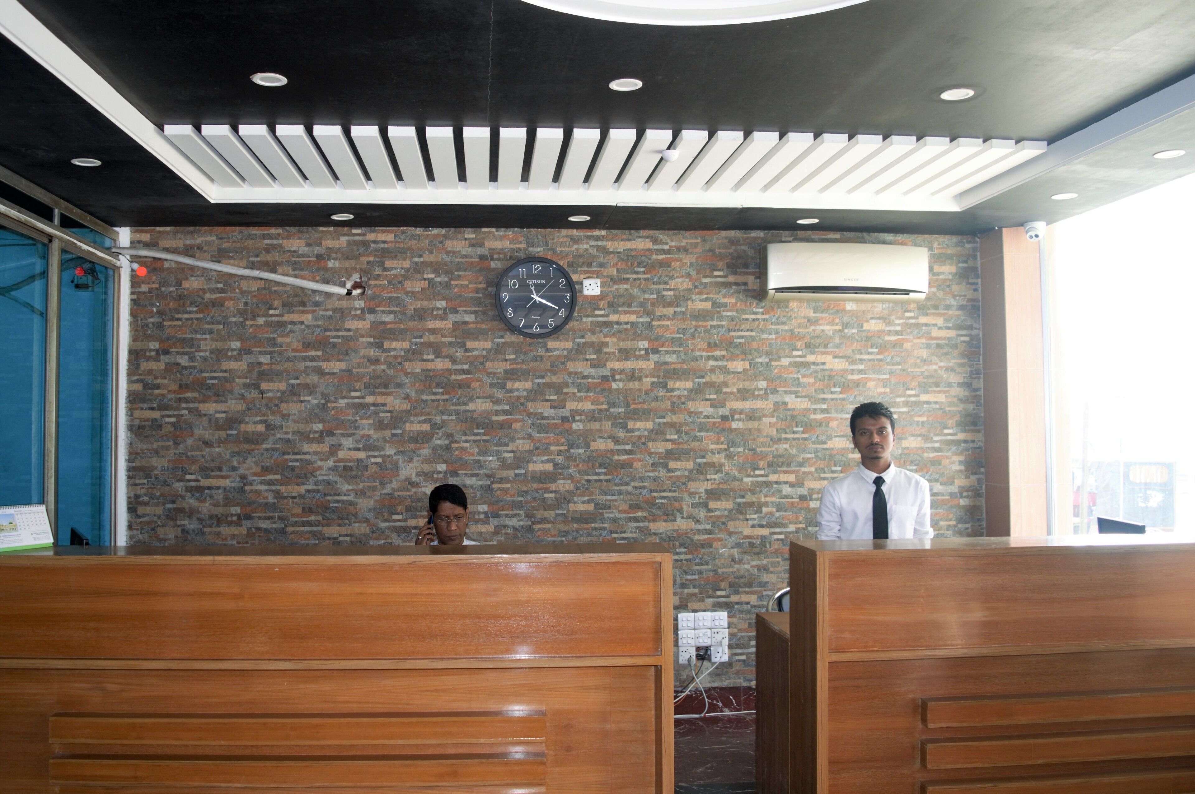 A reception area with a brick wall, a clock, and wooden reception desks.