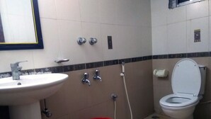 A bathroom with a sink, two faucets, a toilet, and a red bucket. - Hotel Delwar Paradise (Cox's Bazar)