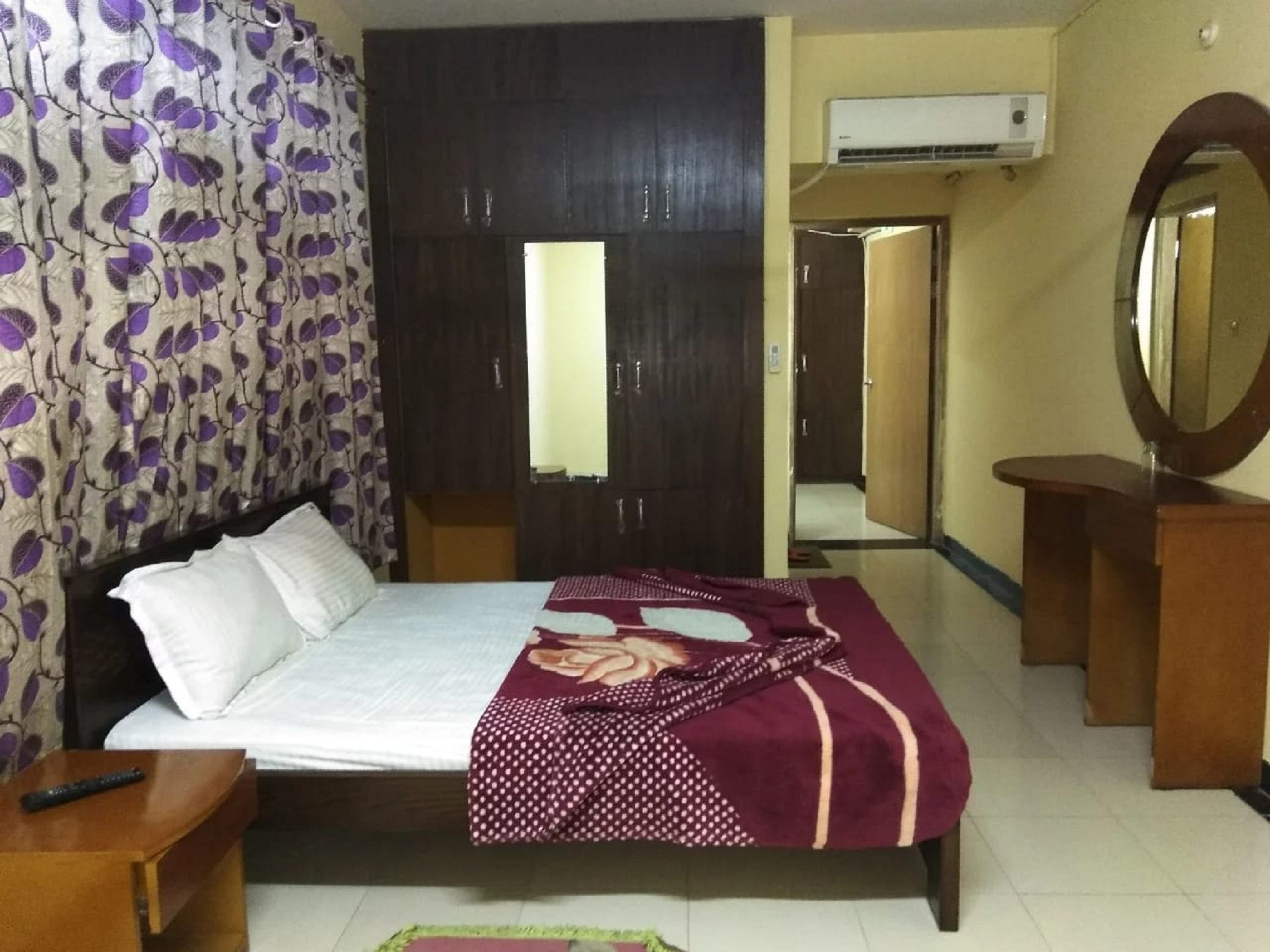 A bedroom with a bed, a wooden wardrobe, a mirror, and an air conditioning unit.