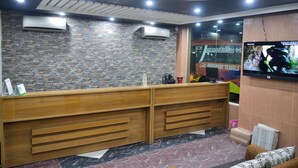 A reception area with a wooden desk, air conditioning units, a television, and a patterned floor. - Hotel Delwar Paradise (Cox's Bazar)