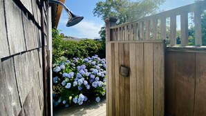 Una terraza de madera con baranda de metal, cerca de madera y jardín con flores de hortensia.