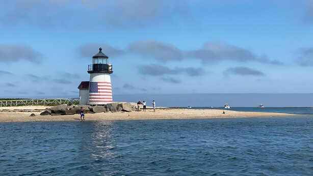 Un faro con un patrón rojo y blanco a rayas, situado junto a un mar tranquilo y una playa de arena.