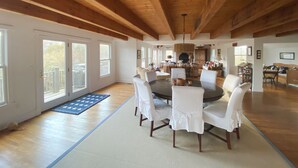 Amplia sala de estar con techo de madera alto, una mesa redonda para comer rodeada de sillas y vistas al exterior a través de grandes ventanales.
