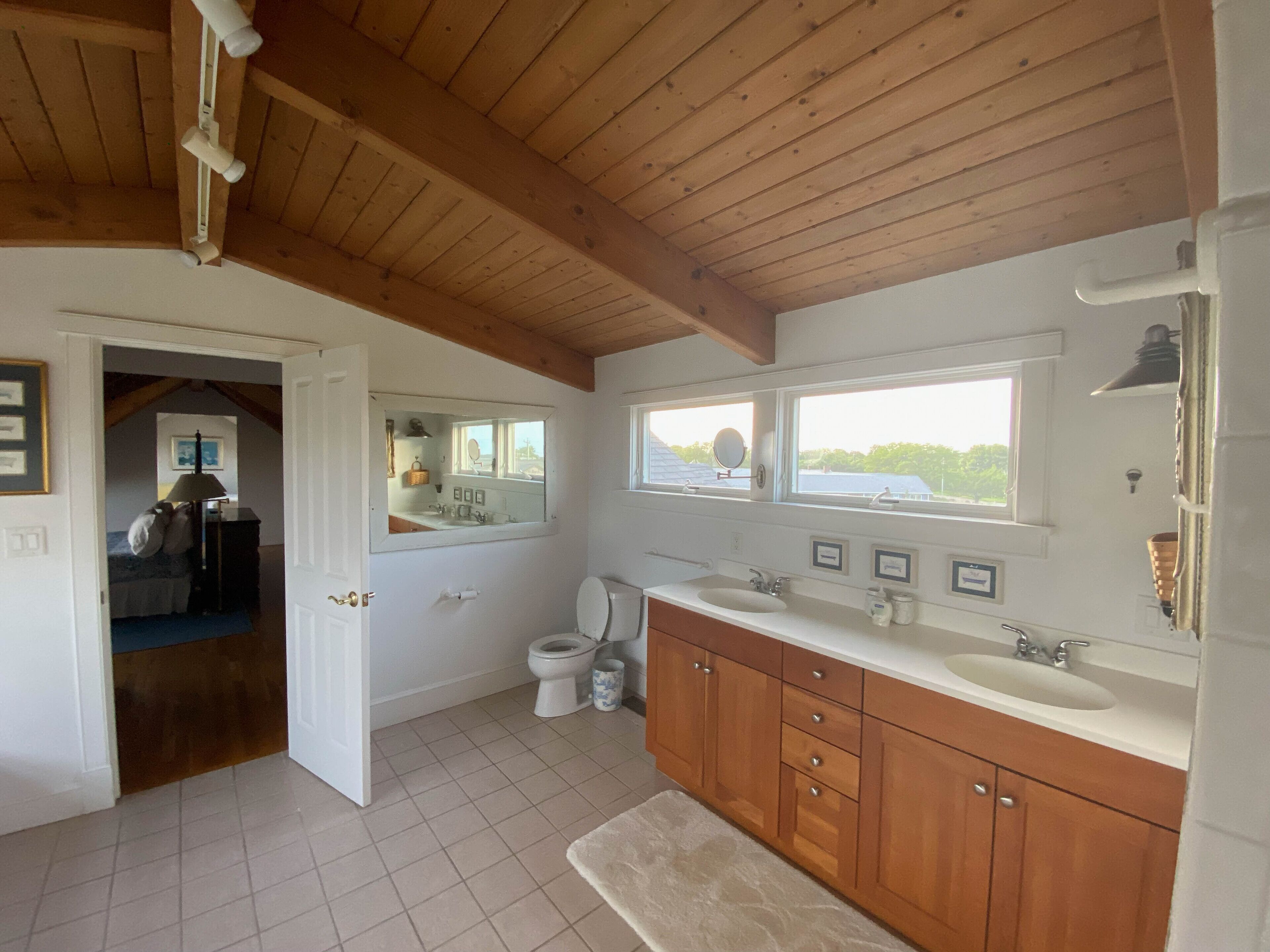 A bathroom with wooden beams, a large mirror, a sink, and a toilet.