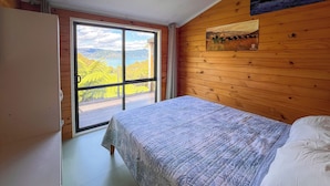 A bedroom with a bed, a wooden wall, a painting, and a view through a glass door. - St Omer Hideaway: Love At First Sight (St Omer Bay)