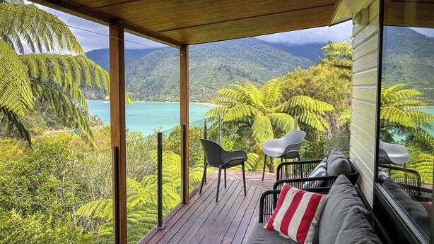 A wooden deck with a sofa and chairs, overlooking a turquoise sea and lush greenery. - St Omer Hideaway: Love At First Sight (St Omer Bay)