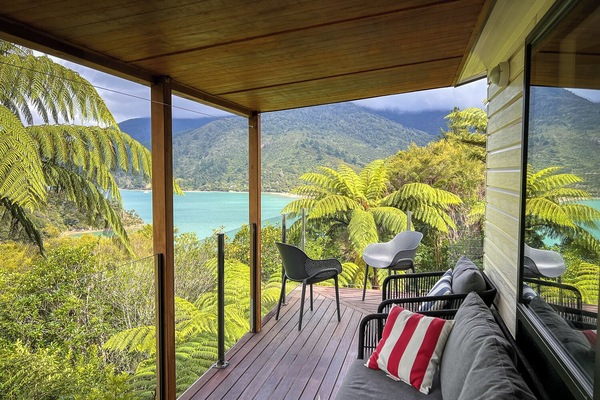 Relax on your private deck overlooking pristine turquoise waters and lush mountains. Your perfect sanctuary awaits with comfortable seating and breathtaking views.