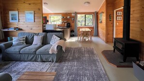A cozy cabin interior with a sofa, dining table, and a wood-burning stove. - St Omer Hideaway: Love At First Sight (St Omer Bay)