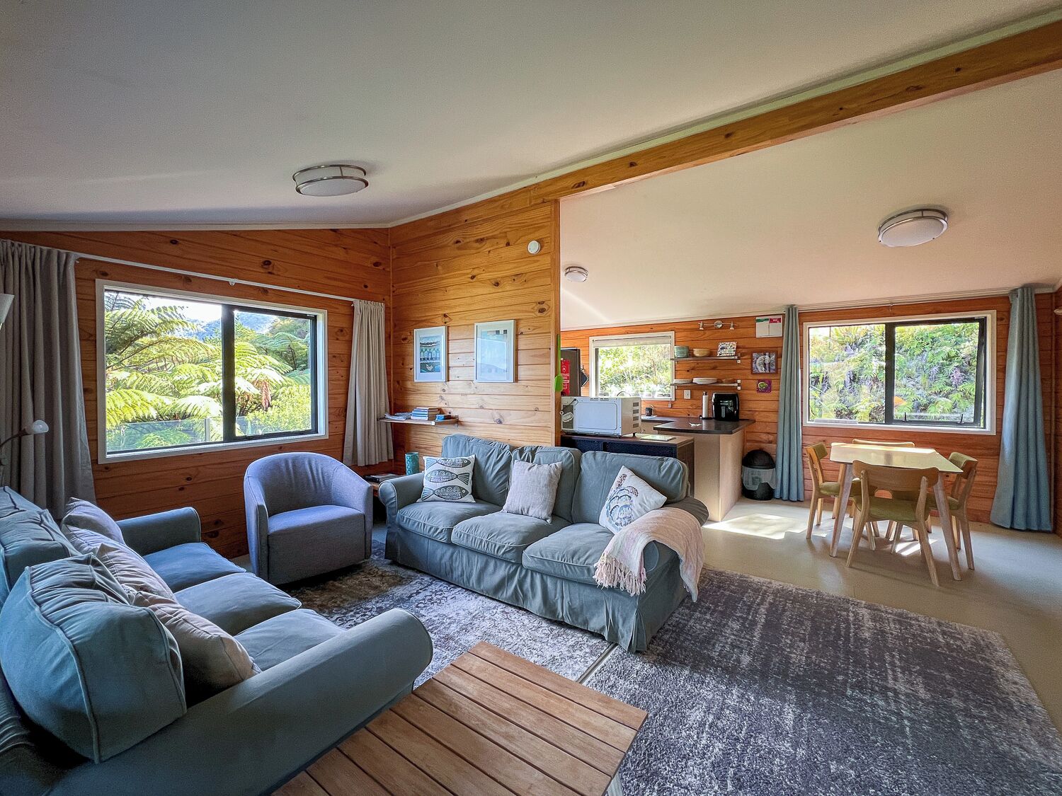 Een gezellig interieur van een chalet met een bank, fauteuil, eettafel en keukenhoek.