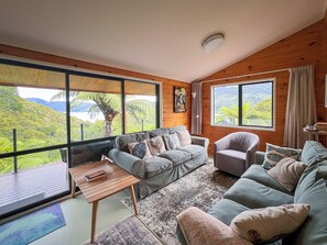 Een ruime woonkamer met een groot raam met uitzicht op weelderige begroeiing en heuvels.