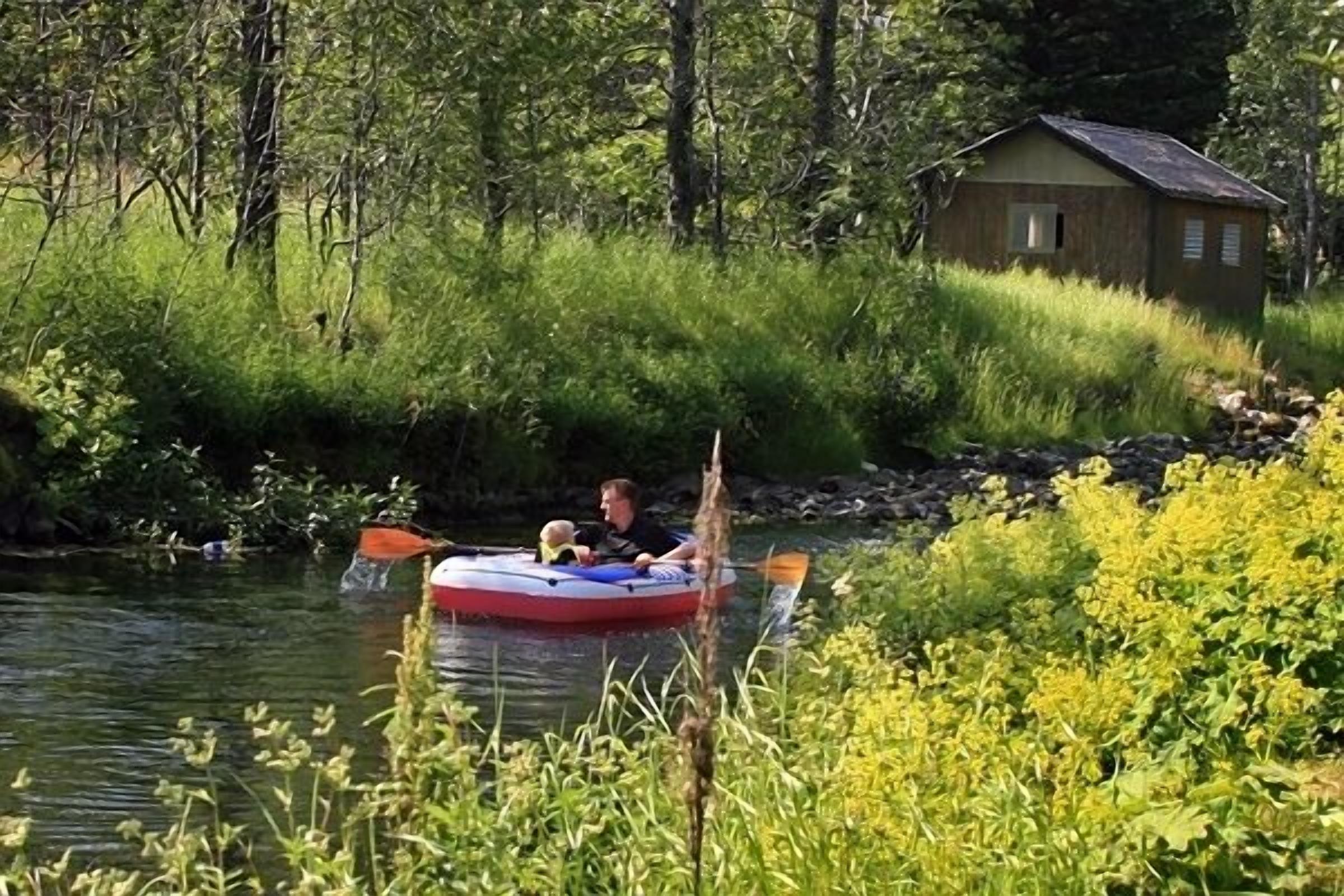 A person in a raft on a river with a cabin in the background.