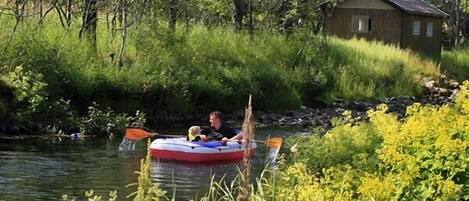 A person in a raft on a river with a cabin in the background.