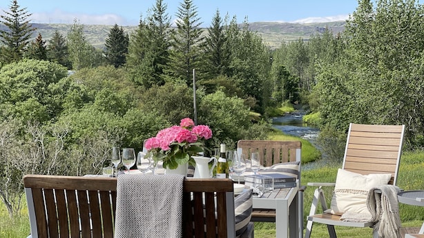 Una terraza con una mesa dispuesta para dos, con vista a un río y colinas boscosas.