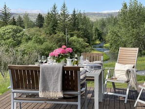 Une terrasse avec une table dressée pour deux personnes, offrant une vue sur une rivière et des collines boisées.