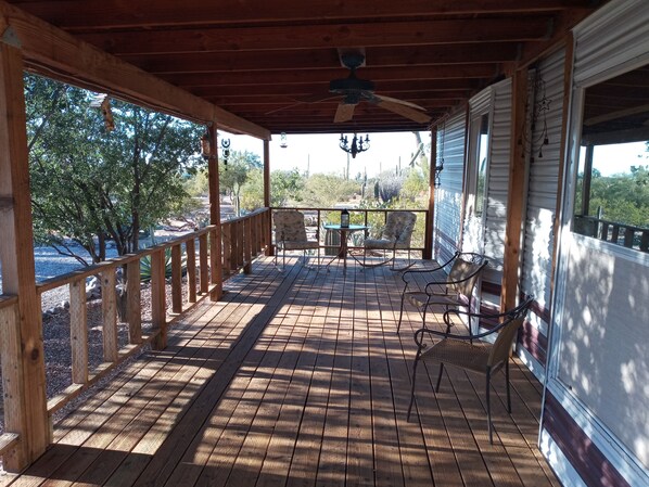 A wooden deck with a ceiling fan, a table with chairs, and a view of trees and cacti.