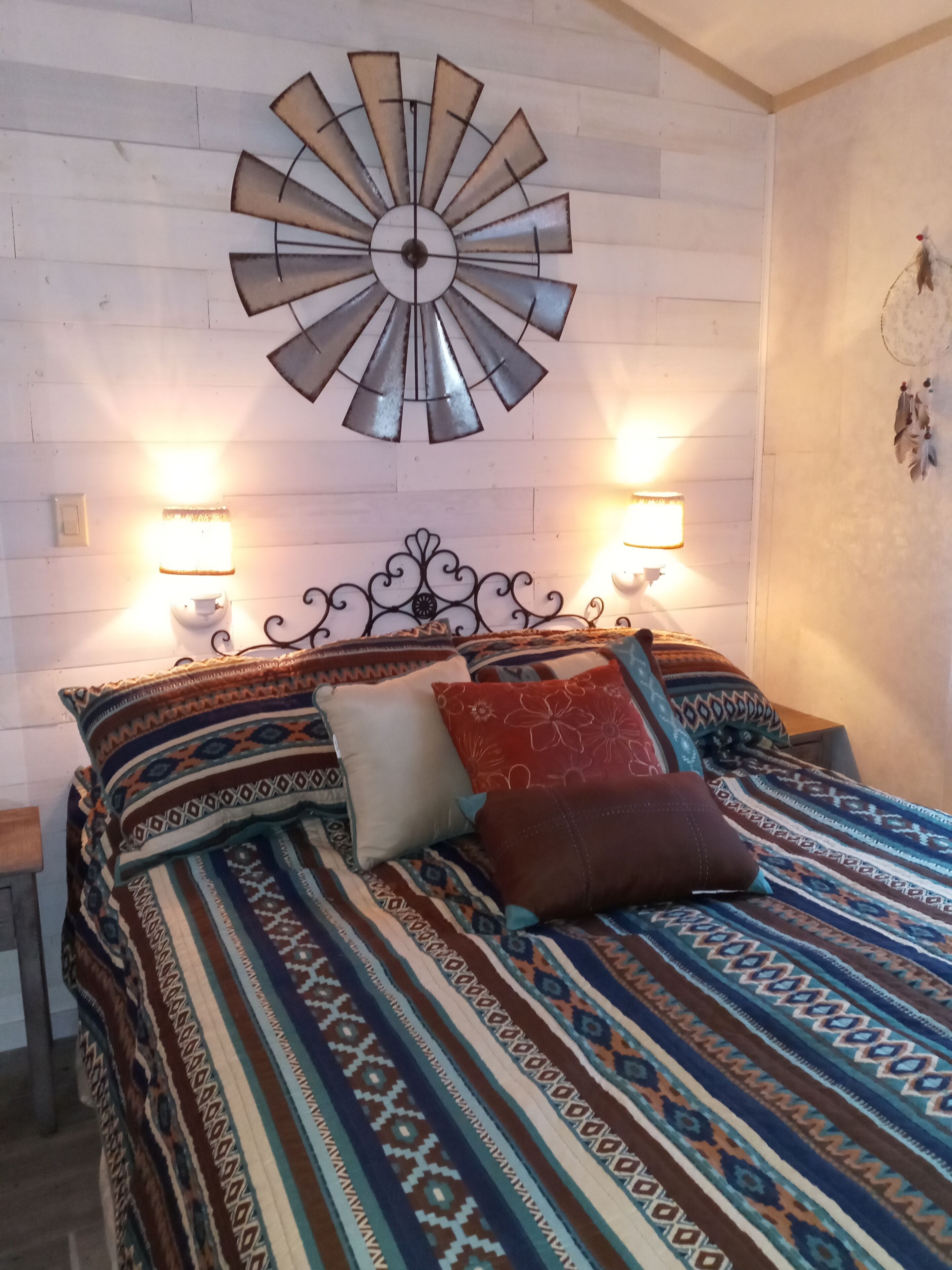 Un lit avec une literie à motifs, deux lampes fixées au mur et un élément décoratif mural.