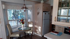 A compact kitchen with a dining table, chairs, a refrigerator, and a small countertop with books.