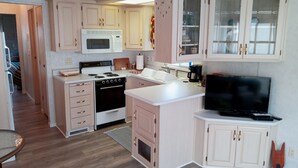 A compact kitchen with a microwave, stove, sink, and a TV.