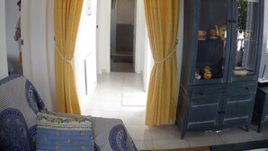 A room with yellow curtains, a patterned sofa, and a dark wooden cabinet with books and decorative items.