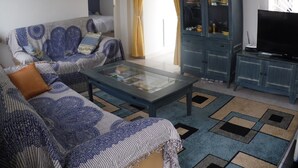 A living room with a sofa, a coffee table, a television, and a cabinet with books.