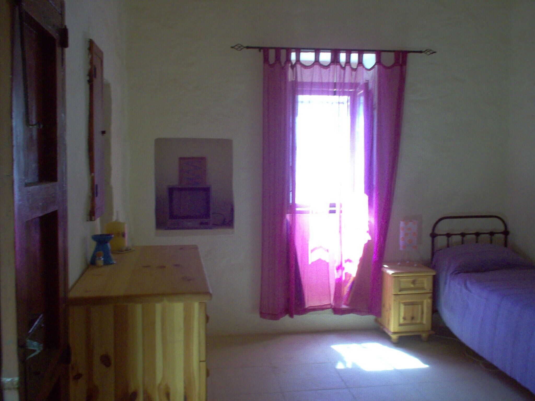Une chambre à coucher avec un lit, une table de chevet, une commode et une fenêtre avec des rideaux.