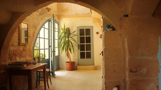 An arched doorway leading to a room with a wooden table, chairs, a potted plant, and a door with a window. - Farmhouse with Own Private Pool Full of Character and Charm (Munxar)
