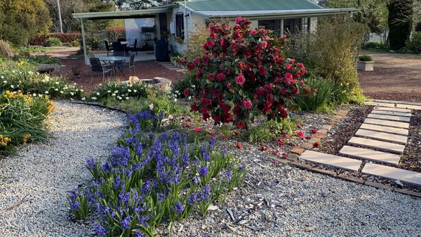 A house with a covered patio, surrounded by a garden with various flowers and a gravel path. - Rydal Cottage (Min 2 night stay) (Rydal)