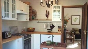 A compact kitchen with white cabinets, a wooden countertop, and a built-in oven. There is a small table with green dishes and a hanging pot rack above the sink. - Rydal Cottage (Min 2 night stay) (Rydal)